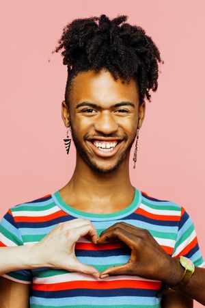 Portrait of a smiling man with earrings and heart shape with multiracial hands