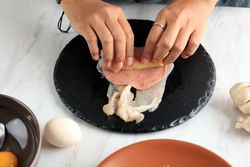 Person rolling salami slice with cheese and chicken breast