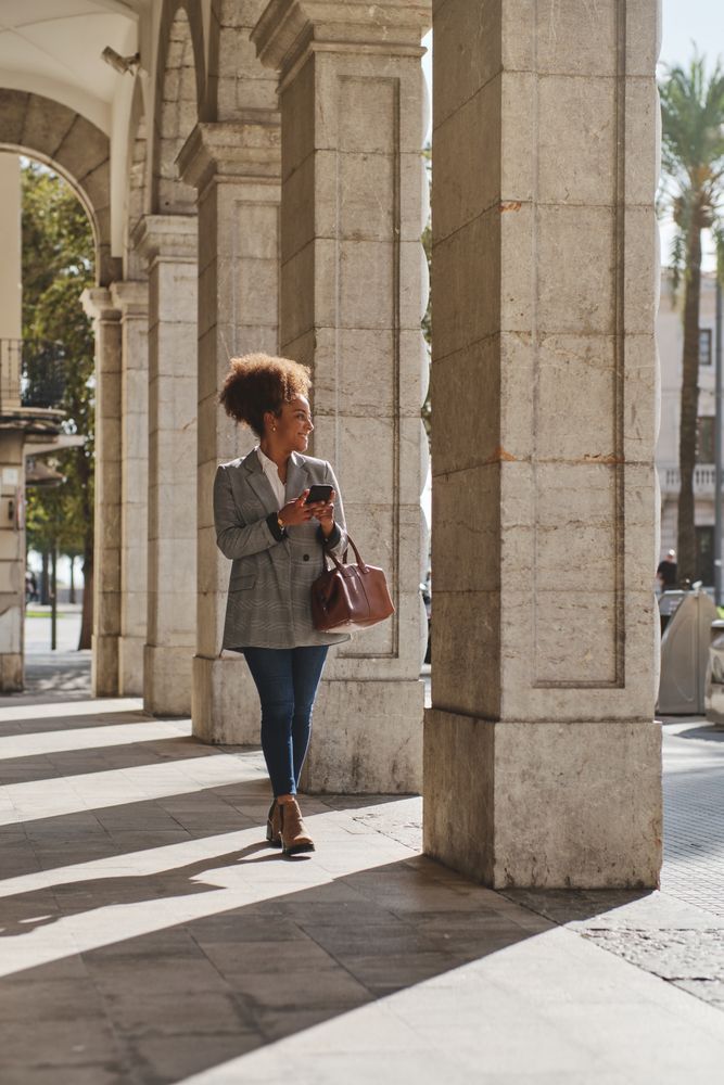 Satisfied Black woman using phone during stroll on street