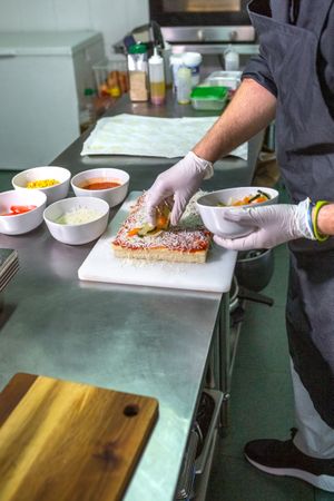 Anonymous male chef adding fresh healthy ingredients to vegetarian pizza in restaurant kitchen