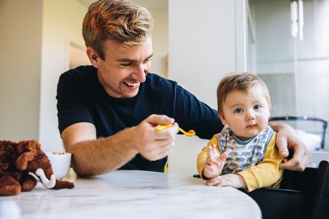 Young father feeding baby toddler with spoon