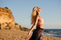 Thin female stretching her arms facing the ocean on beach at sunset