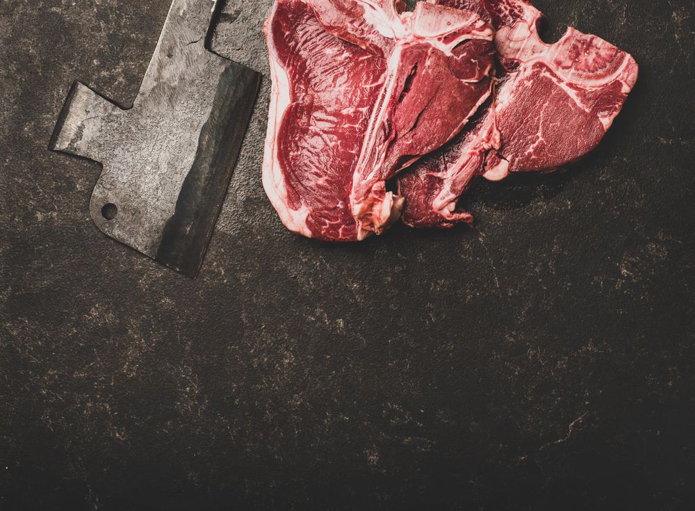 Two T-bone steaks with cleaver on butchers block, square crop with copy space