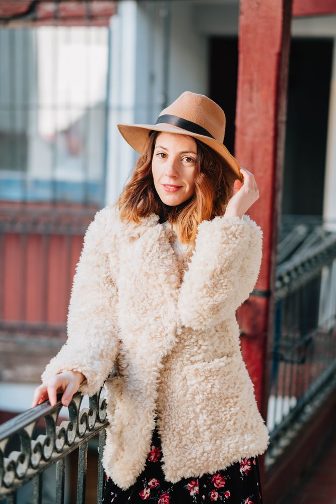 Smiling woman in warm wear standing near building and fence