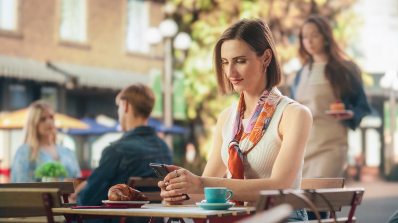 Portrait of a Happy Female Using Smartphone on a Restaurant Terrace, Enjoying a Cup of Coffee. Young Woman Smiling When Receiving a Text, Chatting with Friends Online, Checking Social Network Updates