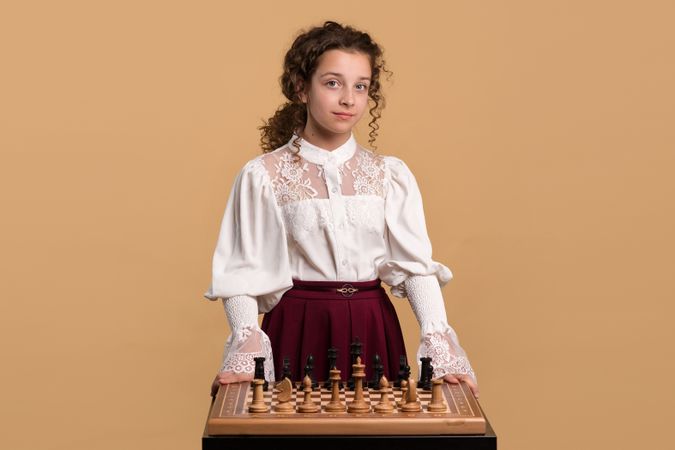 Young girl in white blouse standing behind chessboard