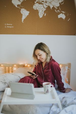 Woman sitting in bed with tablet and looking on smartphone