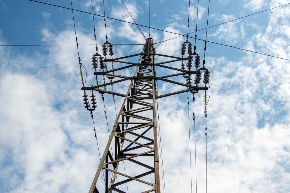 High Voltage Electricity Transmission Tower Against Blue Sky with Clouds