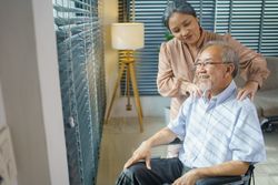 Older Asian woman gives massage to mature husband in wheelchair
