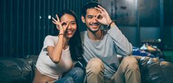 Asian young couple holding hand gesture on eye while sitting together and smiling
