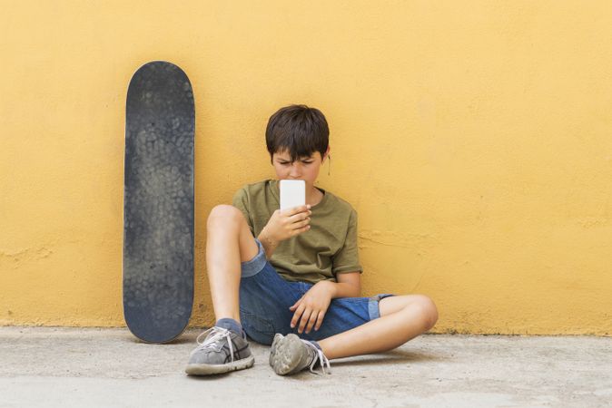 Front view of young boy sitting on ground using a mobile phone