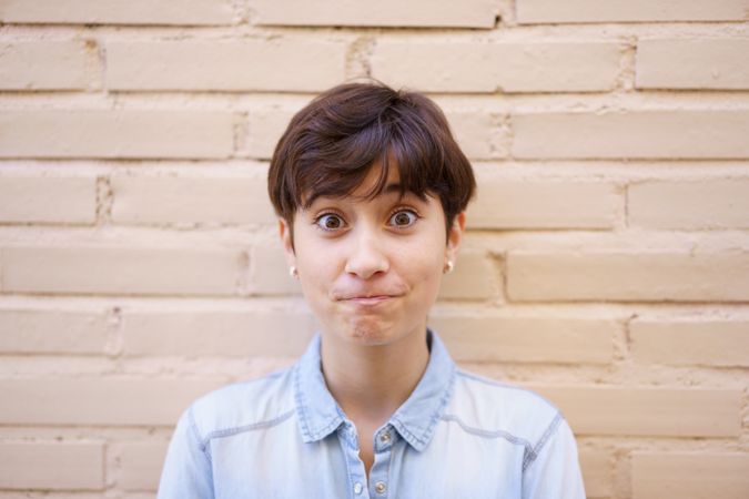 A surprised young woman sporting a trendy short hairstyle stands against a neutral backdrop