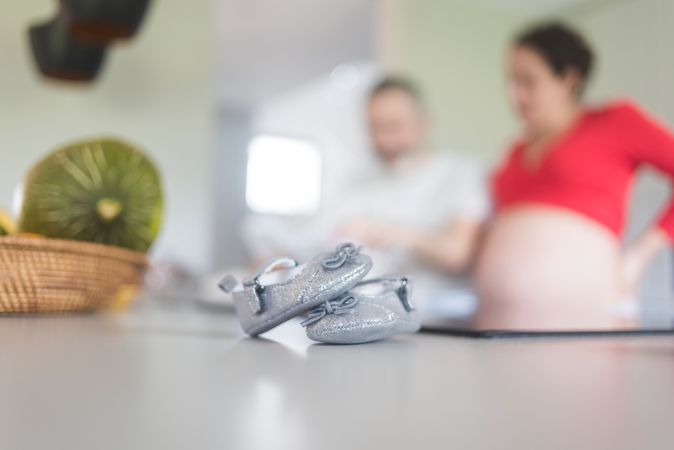 Silver baby shoes in foreground of pregnant woman with man
