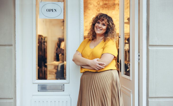 Beautiful curvy woman standing at entrance door of her clothing store