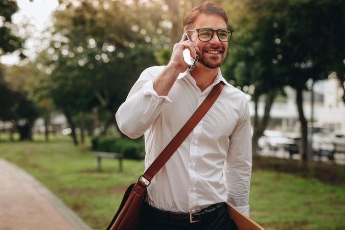 Man carrying office bag talking over mobile phone while walking to office