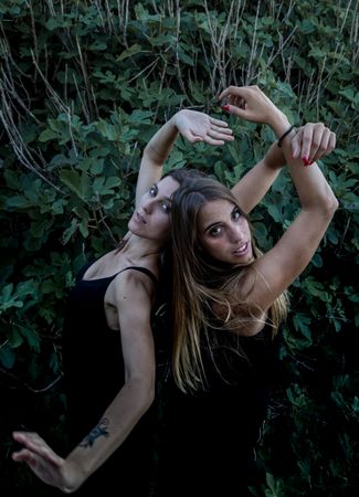 Young women posing near green bush