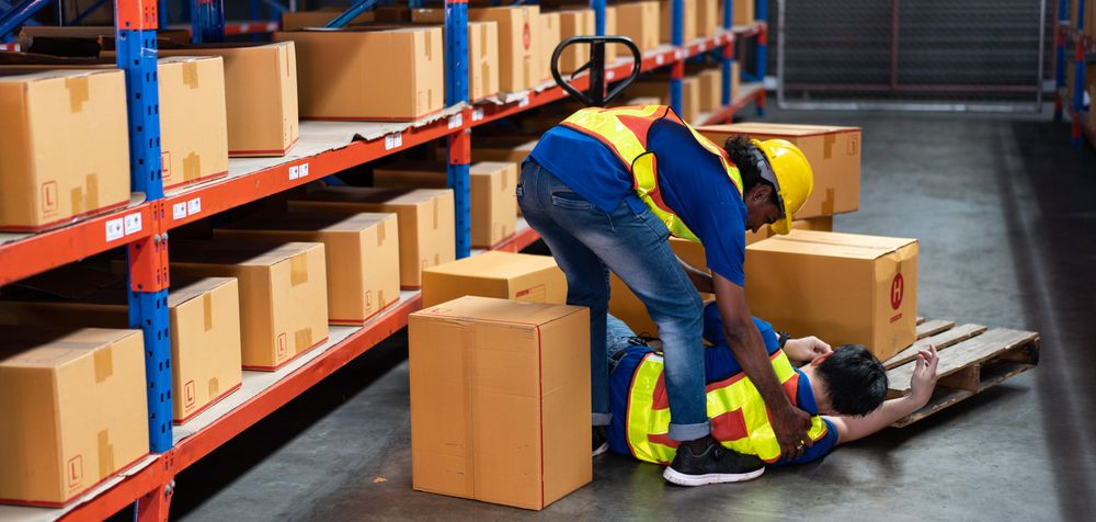 Wide shot of fallen man helped up by colleague in shipping center