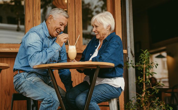 Man and woman sitting at restaurant table laughing and talking with cold coffee on table