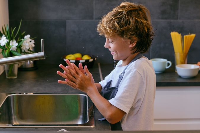 Cheerful boy washing hands in kitchen at home