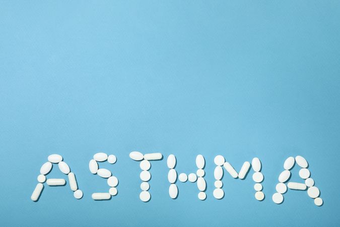 Pills on blue background spelling out “asthma” with copy space