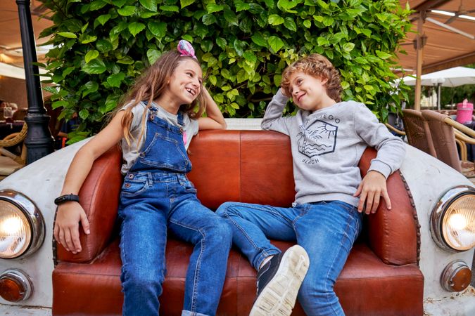 Cheerful kids sitting on retro sofa on summer terrace