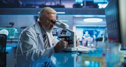 Medical Development Laboratory: Male Scientist Using Microscope, Analyzes Petri Dish Sample.