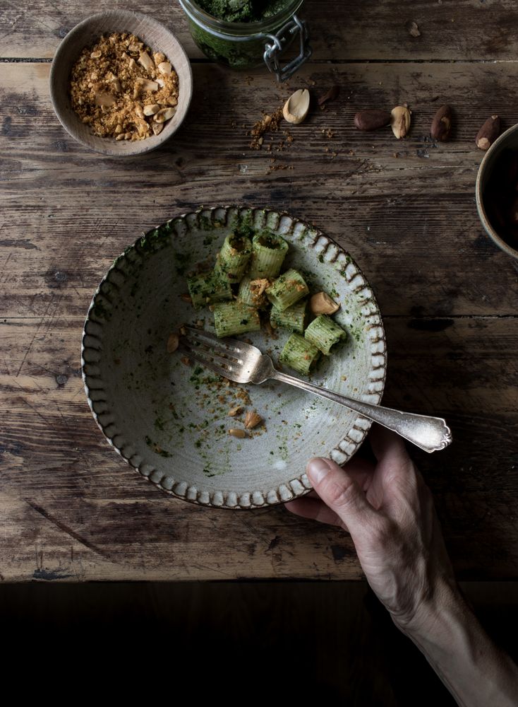 Hands taking pasta paccheri with kale pesto and nuts