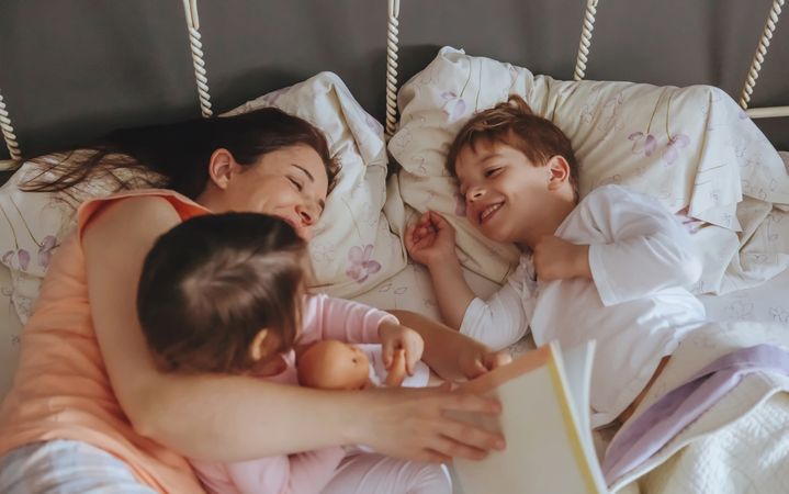 Closeup of woman reading story book to her kids lying in bed