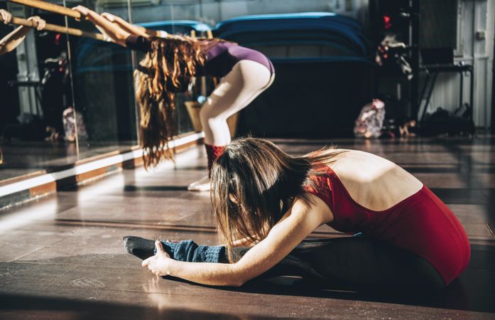Side view of ballerinas warming up and stretching in bright ballet studio.
