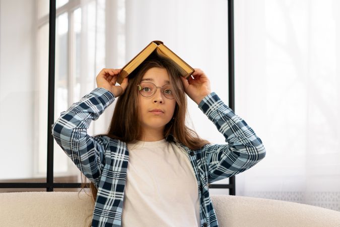 Girl holding open book above head while sitting indoors.