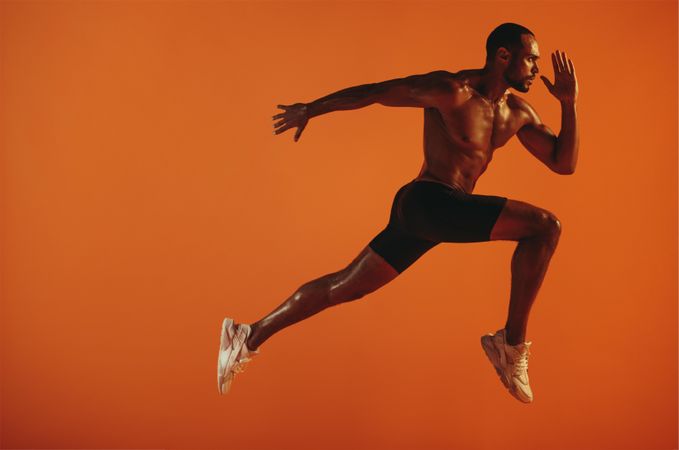 Muscular trainer in running pose while jumping in mid-air