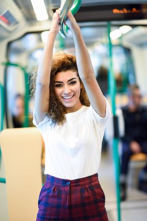 Smiling Arab woman holding bar above head in subway carriage