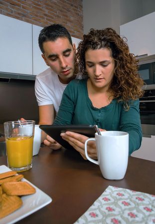Couple reading digital table in kitchen at morning time