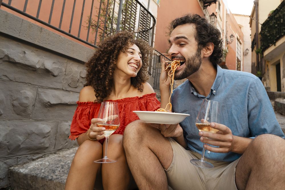 Playful couple eating pasta, woman feeding man