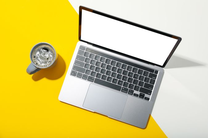 Laptop with mockup screen with mug of coffee on dual tone yellow background