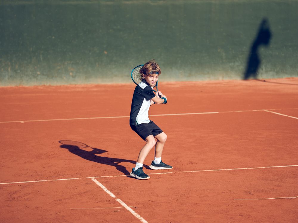 Athletic kid with racket playing tennis on clay court
