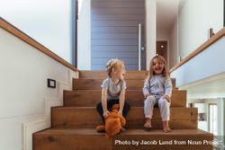 Laughing little boy and girl sitting on wooden stairs with teddy bear 5zRmA5