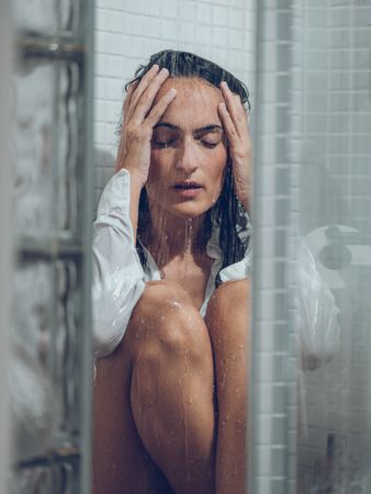Depressed woman in shower under water stream