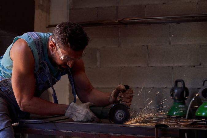Man in protective goggles cutting metal with disk grinder