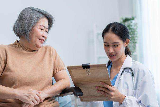 Older Asian woman receiving medical care from doctor with clipboard