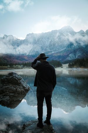 Back view of man with fedora hat standing on rock near lake