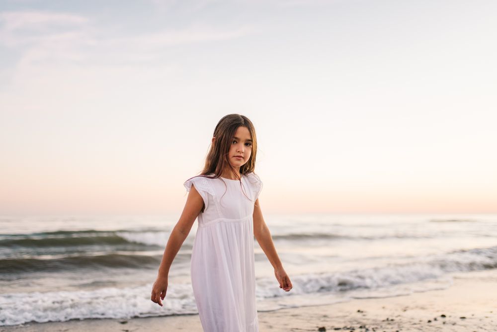 Adorable girl walking and looking at camera on seaside at sunset