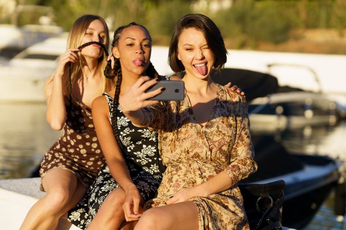 Three women sitting on wharf taking selfie making faces
