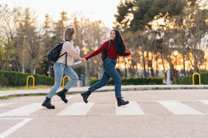 two students crossing crosswalk holding her hands, running and smiling
