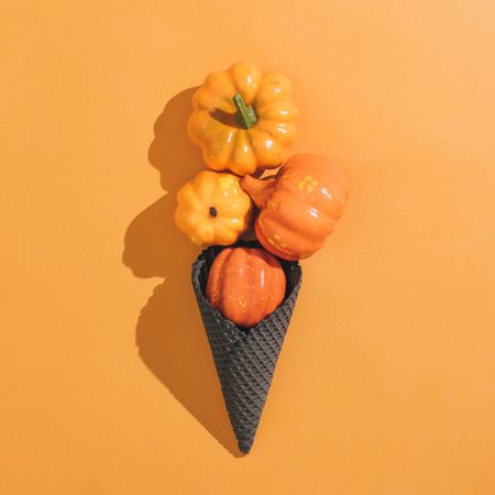 Pumpkins in dark ice cream cone on orange background