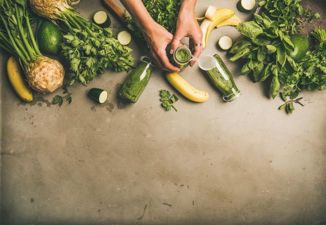 Smoothie ingredients with hands holding bottle, banana, zucchini, on grey table, with copy space