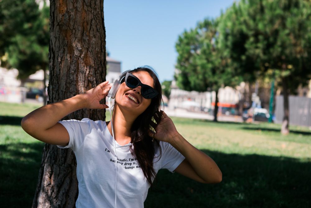 Relaxed trendy woman in headphones resting in park on grass