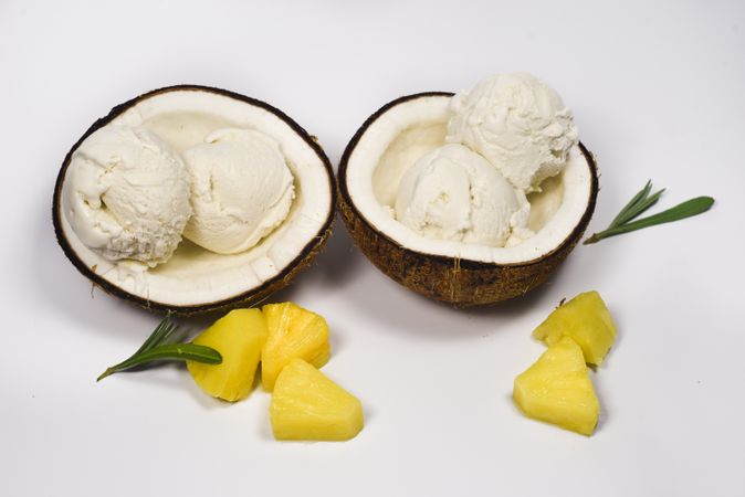 Top view of two coconut halves with ice cream and pineapple fruit chunks