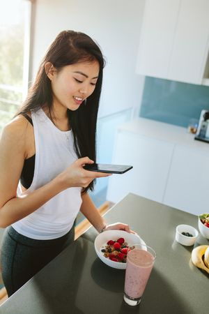 Woman taking picture of her healthy breakfast bowl in kitchen