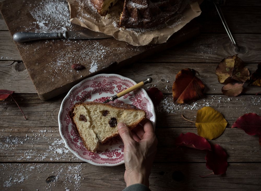 Crop hands holding piece of Kugelhopf near autumn leaves
